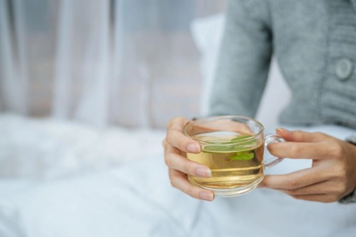 Persona sosteniendo una taza de té riñosan caliente con hojas frescas