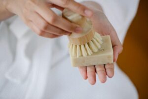 Unas manos femeninas sosteniendo una pastilla de jabón, con una de sus manos sostiene una brocha que frota sobre el jabón