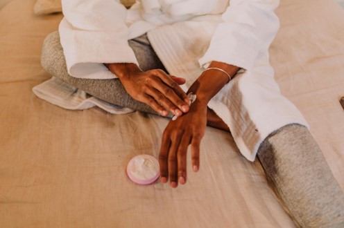 Una persona sentada sobre una cama, aplicándose crema de colágeno y elastina en la mano