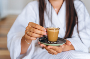 Mujer sosteniendo una pequeña taza de café keto sobre un plato negro