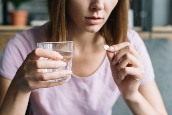 Mujer tomando una pastilla con agua, promoviendo el consumo de gluconato de potasio