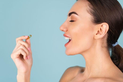Mujer joven sonriente sosteniendo cápsula de vitaminas ACD lista para tomar su suplemento diario