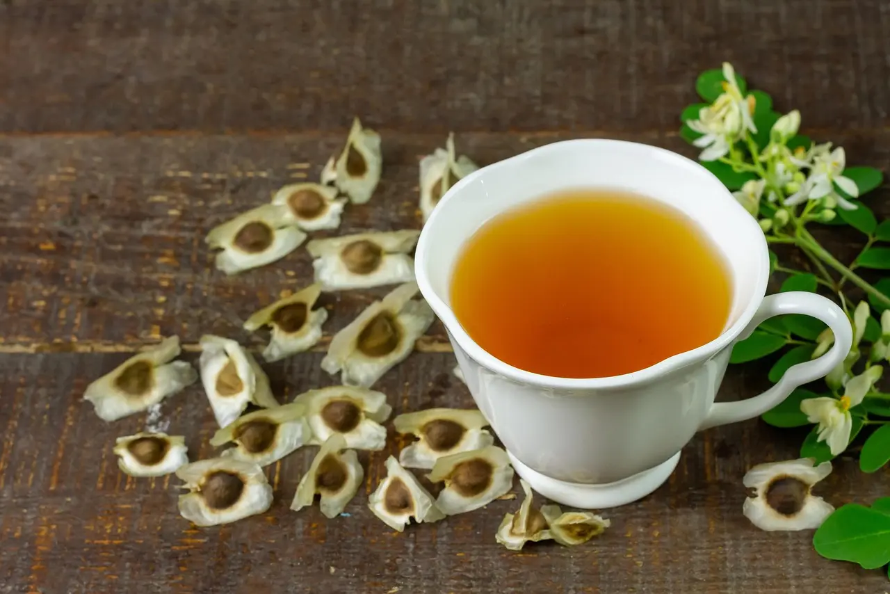 Taza de té de moringa junto a semillas y flores de moringa