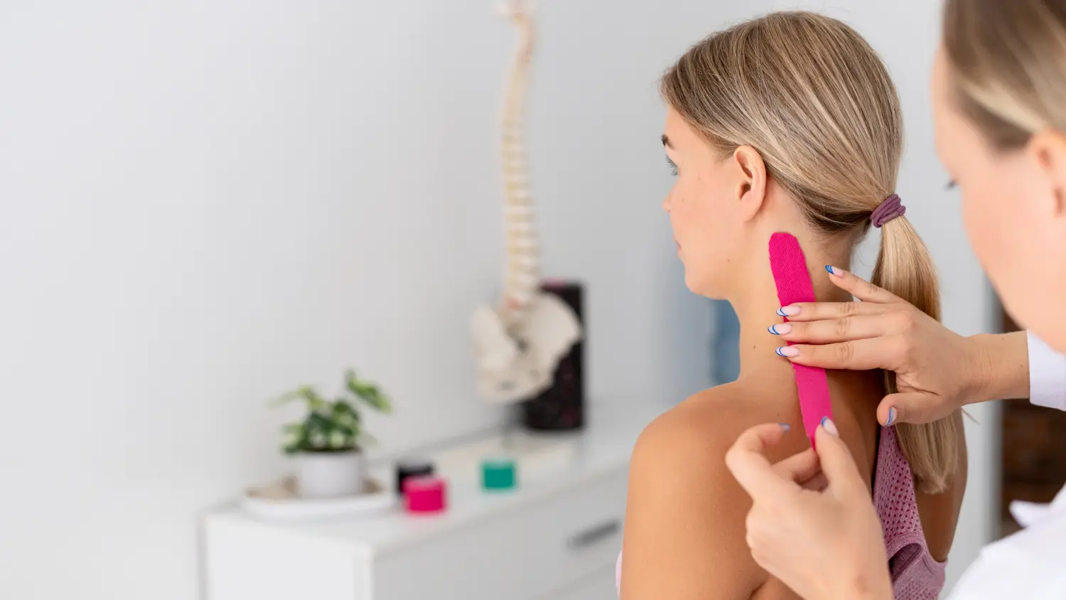 Fisioterapeuta femenina aplicando un vendaje neuromuscular en forma de I en el cuello a una paciente femenina