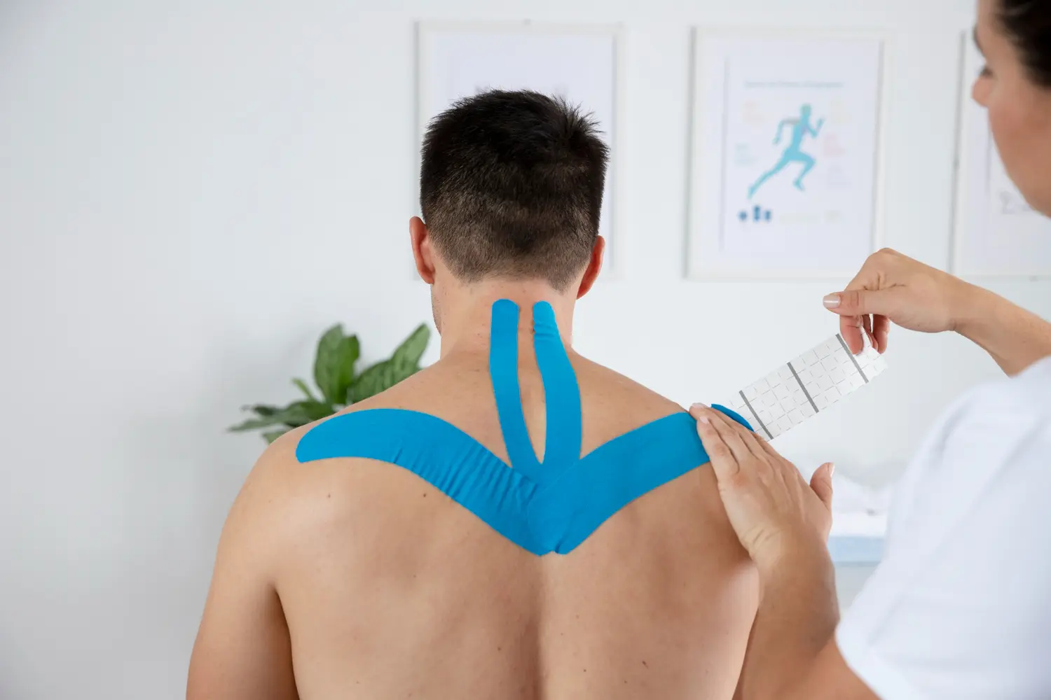 Fisioterapeuta femenina aplicando un vendaje neuromuscular en forma de X en la espalda de un paciente masculino