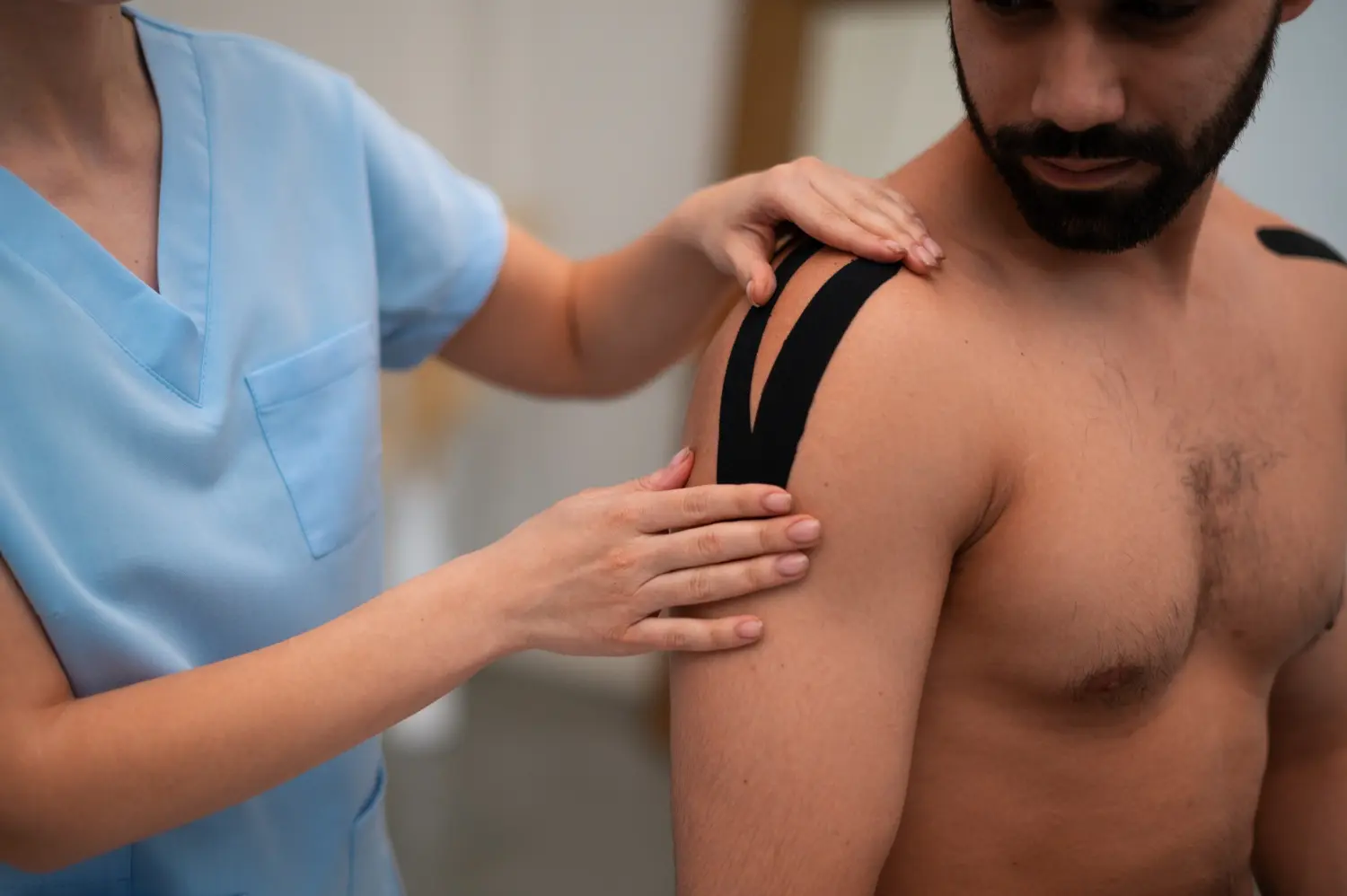 Fisioterapeuta femenina aplicando un vendaje neuromuscular en hombro en forma de Y a un paciente masculino